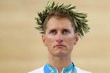 A male cyclist wears an olive wreath on his head. He has a gold medal around his neck. 