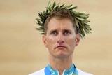 A male cyclist wears an olive wreath on his head. He has a gold medal around his neck. 