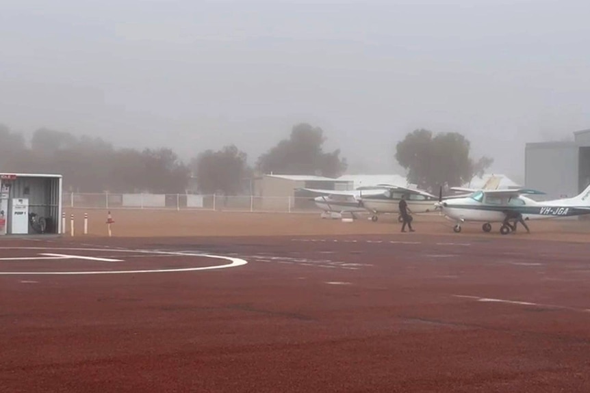 Ground crew carry out checks on light planes at an outback airstrip blanketed in fog.