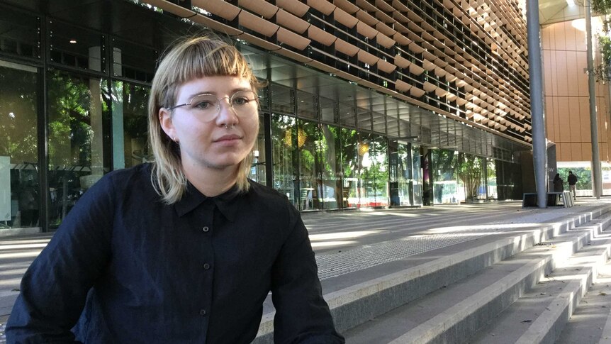 Anna Hush from End Rape on Campus sits on concrete steps outside a modern building
