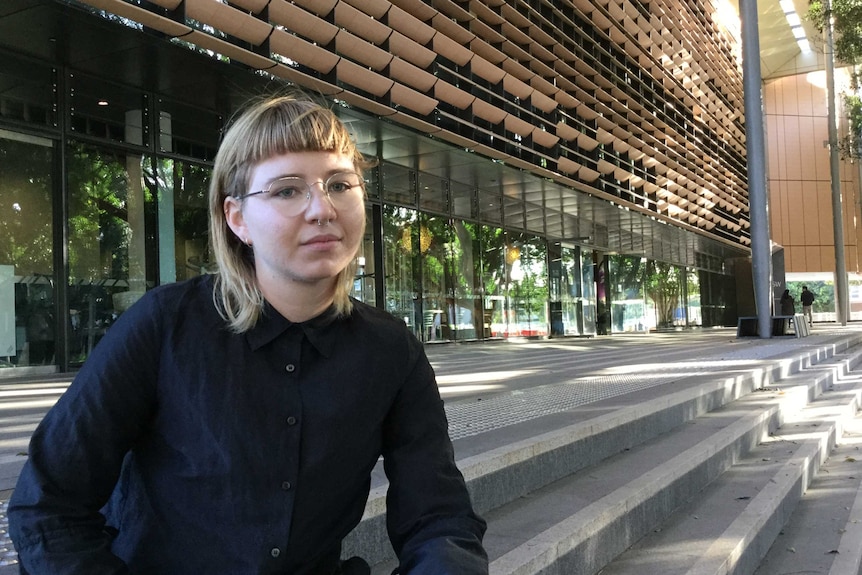 Anna Hush from End Rape on Campus sits on concrete steps outside a modern building