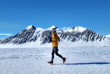 Woman in winter-wear running on snow with ice-capped mountain in background and clear blue sky