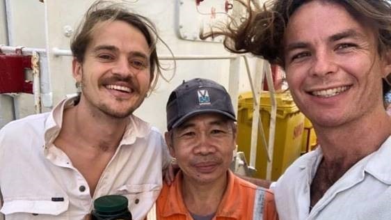 A man in an orange high-vis shirt and cap is holding a jar of manuka honey. He is standing between two taller man.