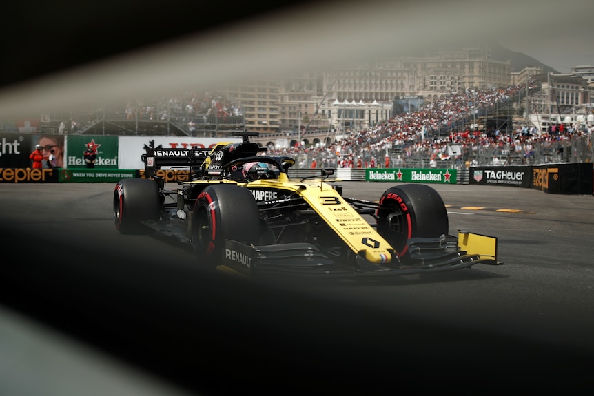 Daniel Ricciardo drives his yellow Renault F1 car in Monaco as seen through a safety barrier