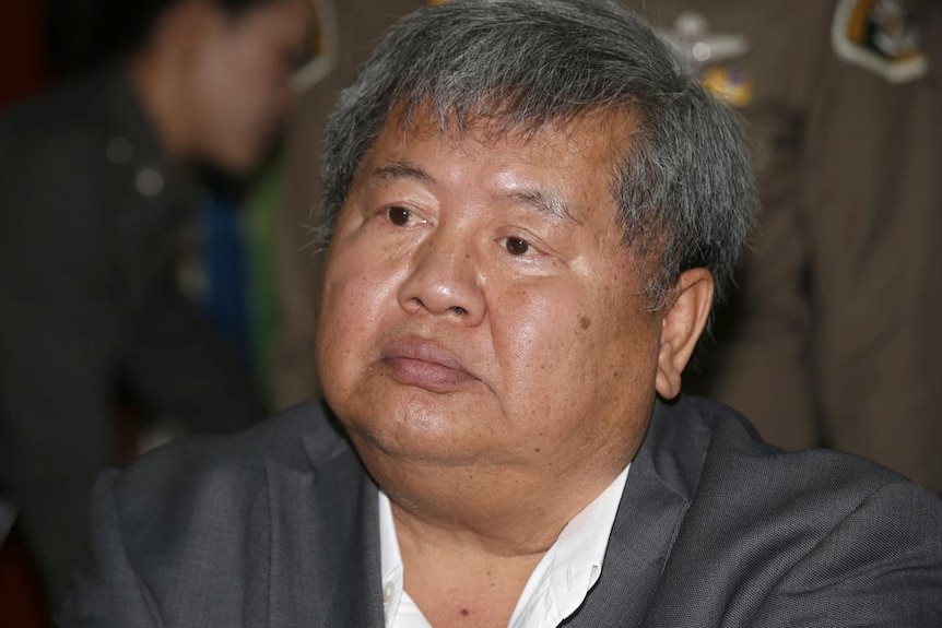 a thai man with short grey hair and a round face wearing a grey suit 