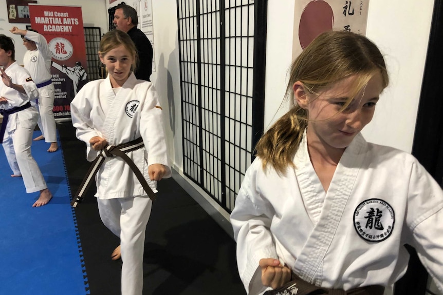 Two girls step forward with an arm in a martial arts class, wearing their white uniforms.