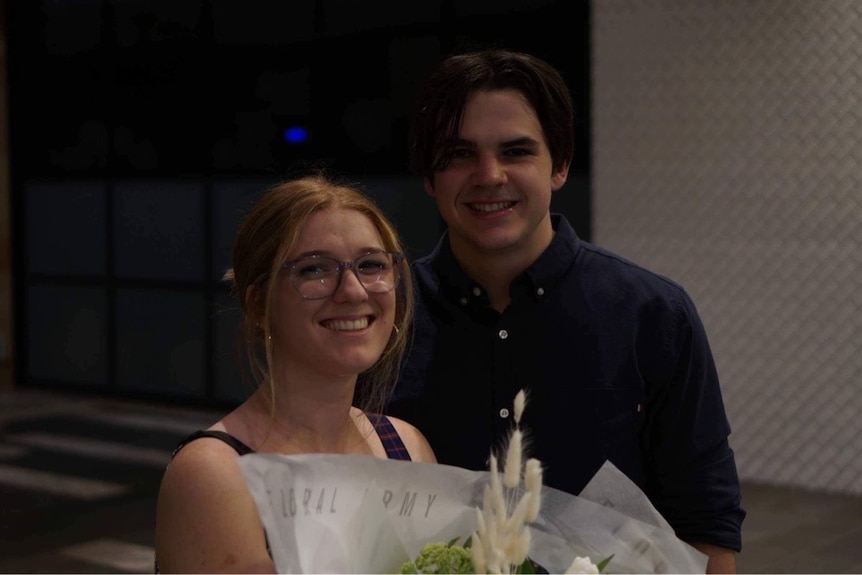 A man and a woman smiling while the woman holds flowers. 