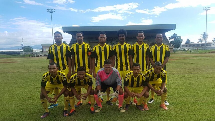 Eleven players from the Papaka pose for a photo on a football pitch.