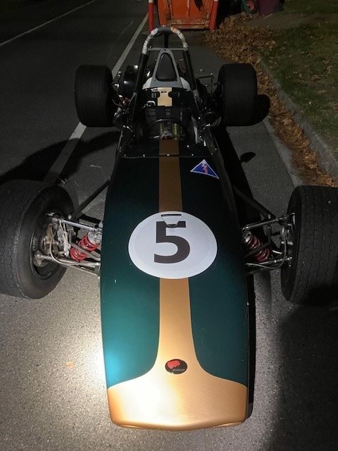 A green and gold race car with the number five on it, sitting stationary on a concrete road. 
