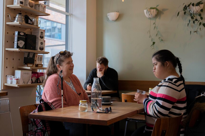 A mother and daughter chat and smile while seated at a cafe table.