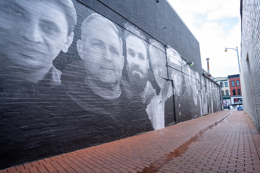 Grey scale faces painted on a black brick wall in a laneway