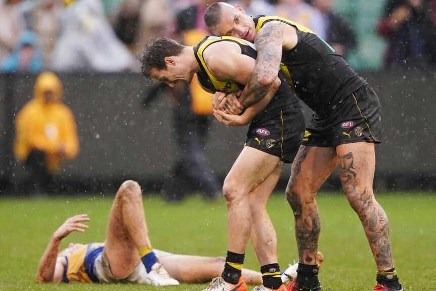 Dustin Martin hugs Kane Lambert from behind. An Eagles player lays on the ground behind them.