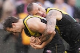 Dustin Martin hugs Kane Lambert from behind. An Eagles player lays on the ground behind them.