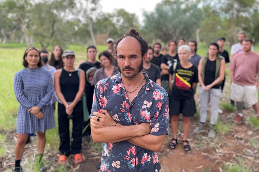 a man with facial hair and a bun wearing a floral shirt in front of a group of people