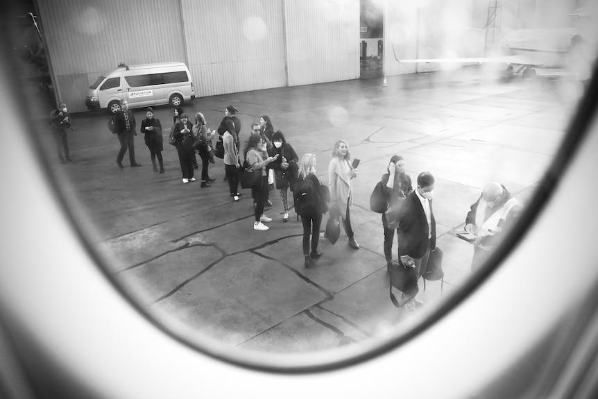 Black and white photo shot through aeroplane window of media queuing to board.