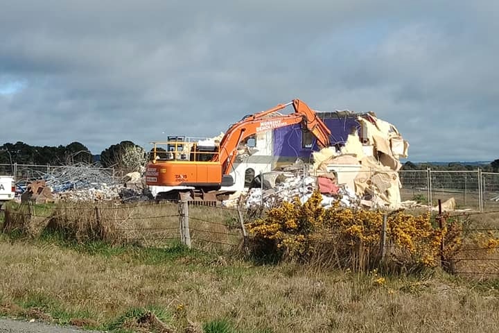 An orange crane eats into a monolithic dome structure that is 3/4 demolished.
