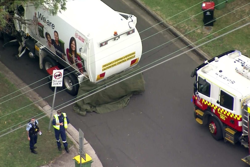 emergency services around a garbage truck which has partially been covered my a blanket