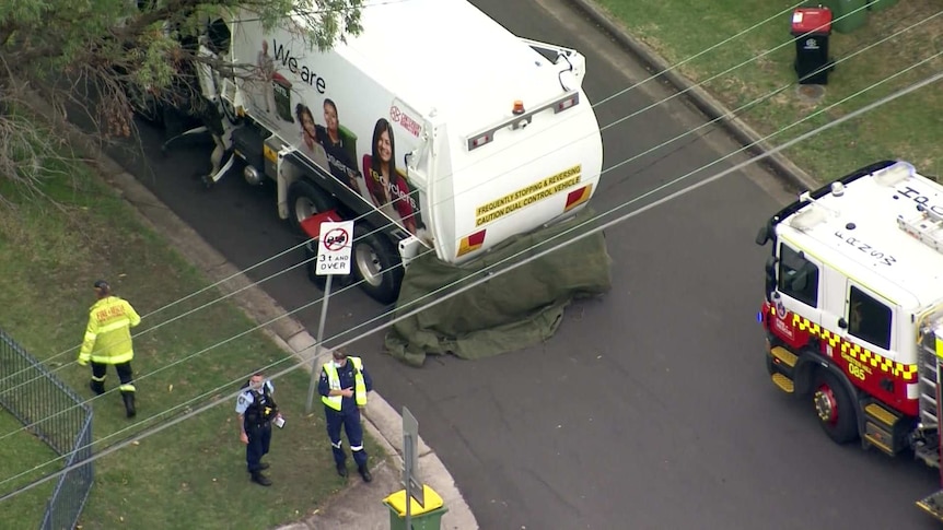 emergency services around a garbage truck which has partially been covered my a blanket