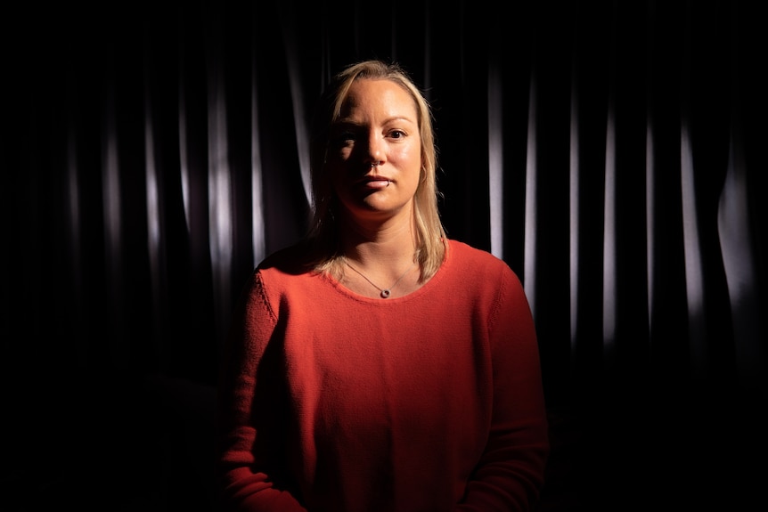 A dark background of curtains are behind Jessie Orrell as she looks at the camera.