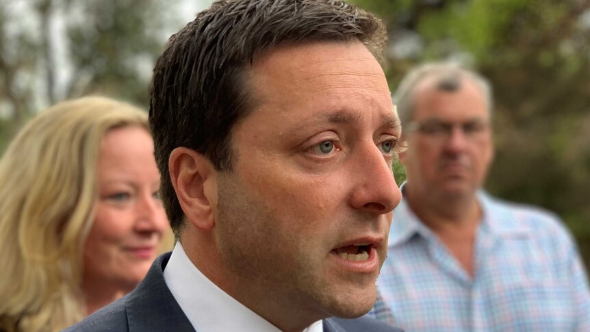 Matthew Guy speaks with a woman and a man standing behind him.