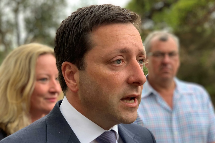 Matthew Guy speaks with a woman and a man standing behind him.