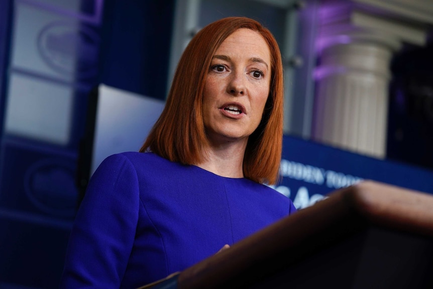 Jen Psaki stands a wooden lectern.