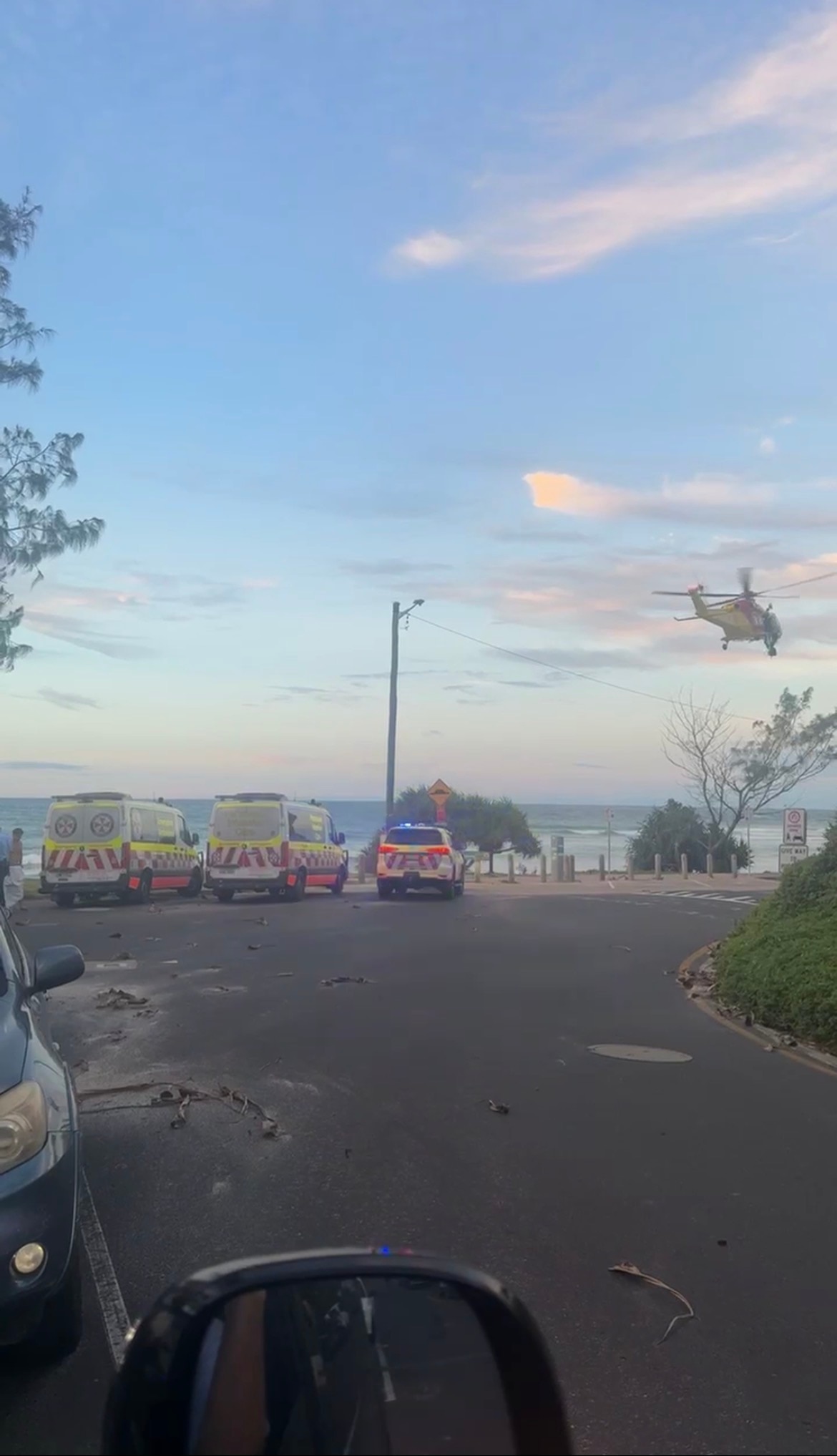 Ambulances, police cars parked at a beach with a rescue helicopter flying above.
