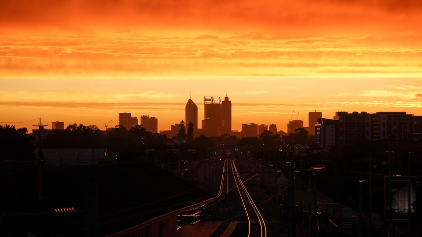 A bright orange sky above the silhouette of Perth city buildings.