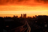 A bright orange sky above the silhouette of Perth city buildings.