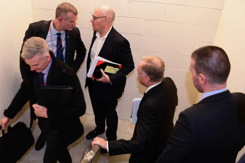 A group of men in suits in a concrete stairwell.