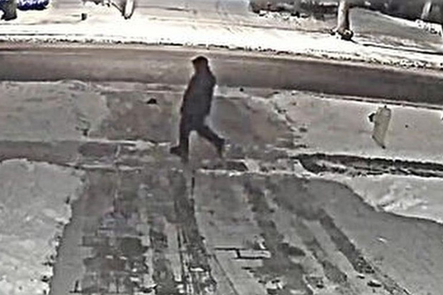 A CCTV screenshot of a person walking past a snowy driveway at night