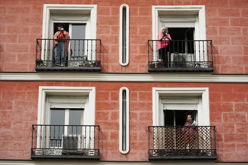 A wide image of an apartment block shows women on three separate balconies banging on saucepans.
