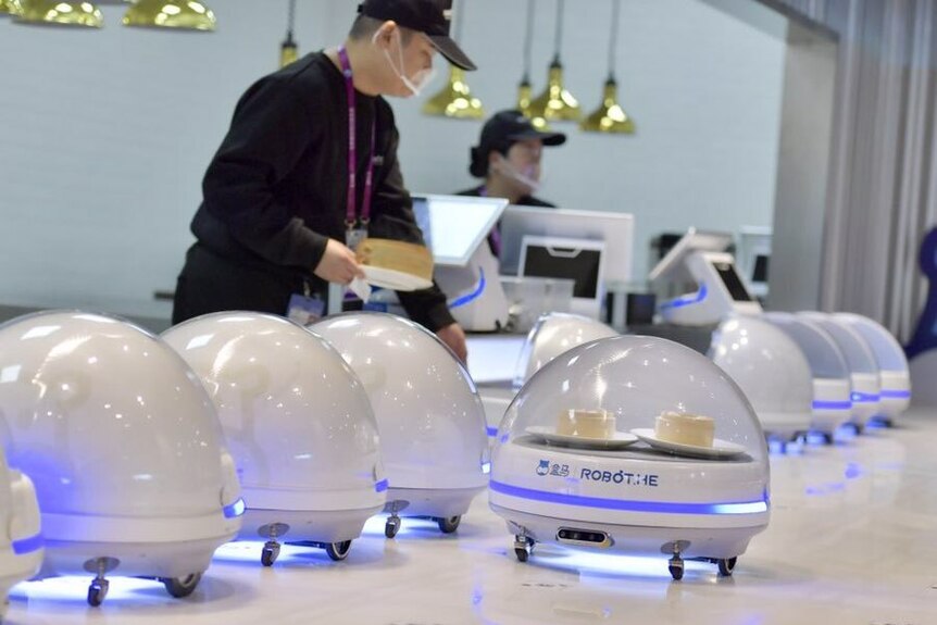 Dome-shaped robotic waiters carrying various dishes travel down a table.