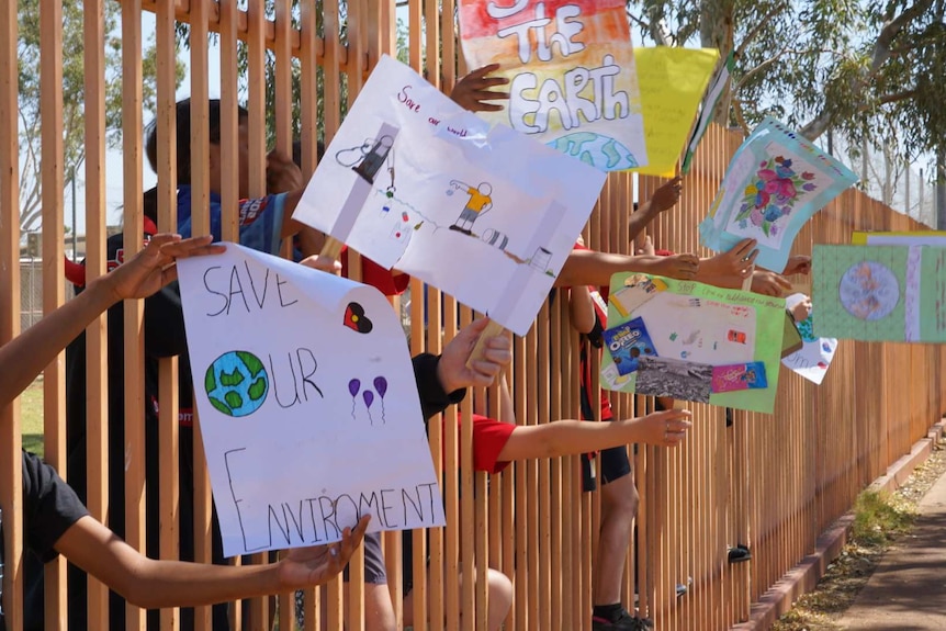 Students' hands reach through a fence to display climate protest signs