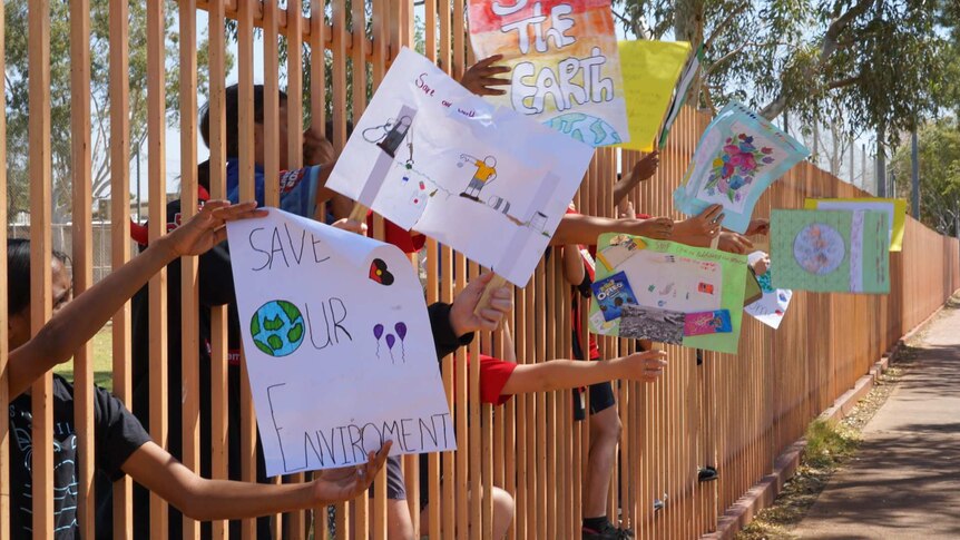Students' hands reach through a fence to display climate protest signs