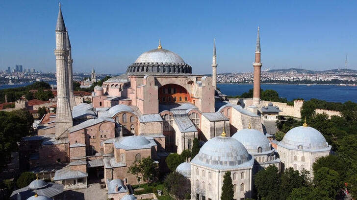 A view from the outside of Hagia Sophia under a blue sky, beach in background.