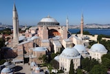 A view from the outside of Hagia Sophia under a blue sky, beach in background.