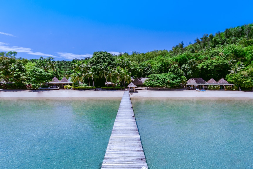 A wooden walkway to a tropical island resort over water