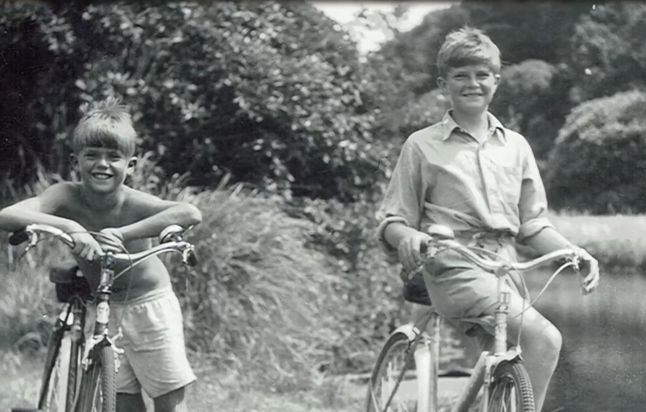 Black and white image two boys on bikes, smiling 