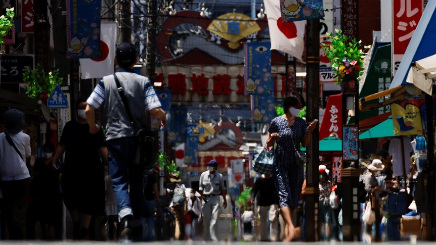 Pedestrians walking on a Japanese street with flags and signs on either side.
