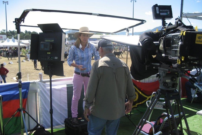 Pip Courtney surrounded by lights, camera and reflector boards standing in front of cows in arena.