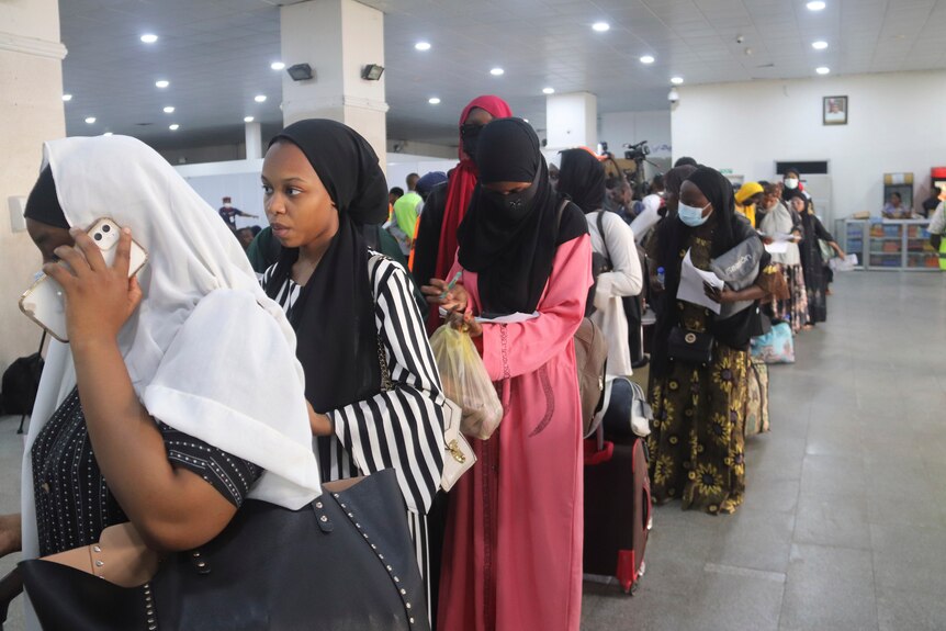 A row of Nigerian women wait in line at airport.