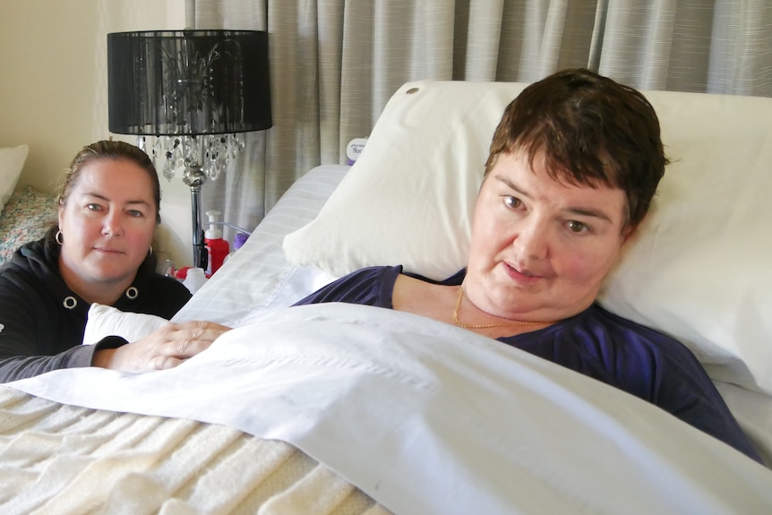 A woman in a bed with another woman sitting next to her.