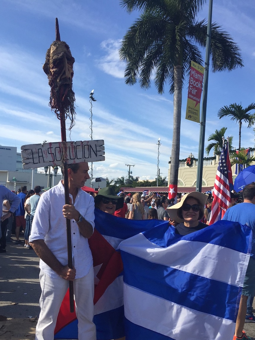 People celebrating in Little Havana hold flags, model of Castro's head impaled on a spike.