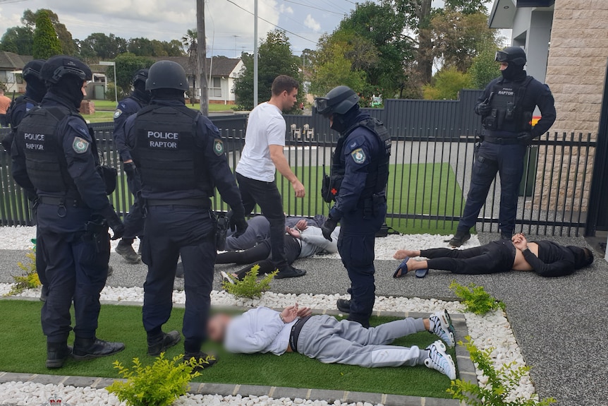 Police standing over other men who are lying on the ground outside a residential home 