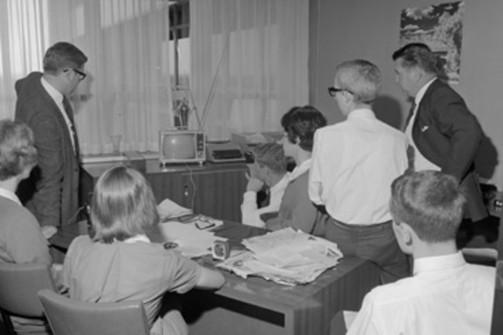 A crowd gathers around a very small TV