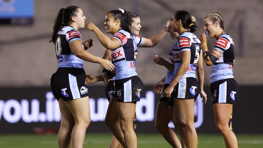 A group of Cronulla NRLW players smile and embrace at the end of a game.