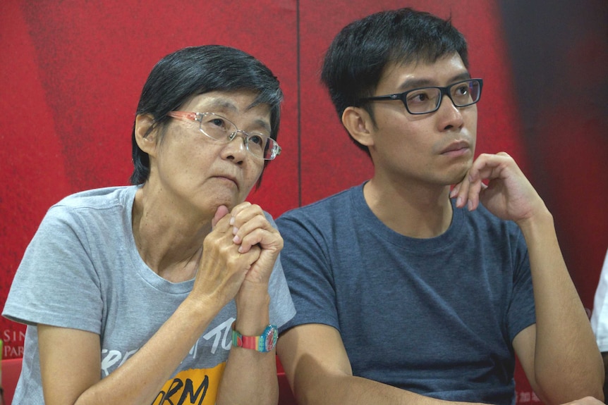 A woman and man sit in front of a red backdrop.