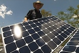 A man holds up a solar panel while installing it on a roof