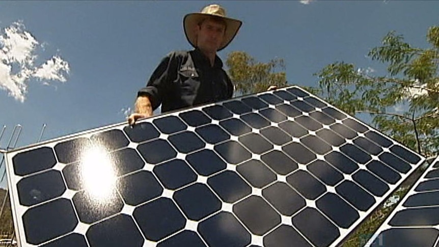 A man installs a solar panel on a roof.